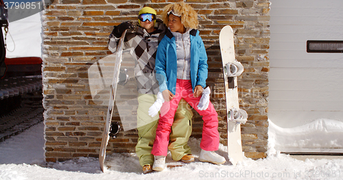 Image of Close couple posing with snowboards against garage