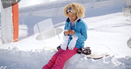 Image of Woman sitting on snowbank texting