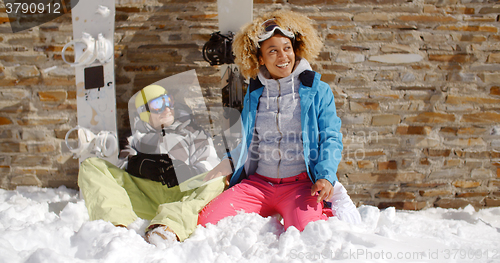 Image of Laughing woman sitting next to friend in snow