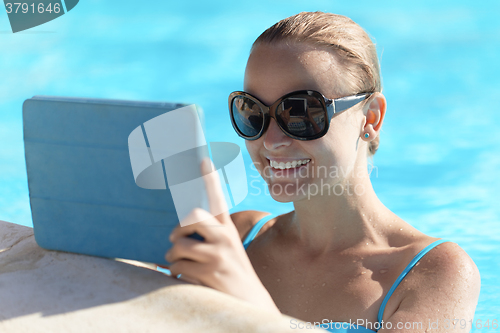 Image of Young woman in a pool using tablet computer