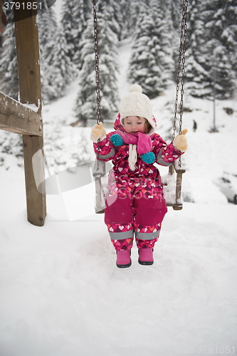 Image of little girl at snowy winter day swing in park