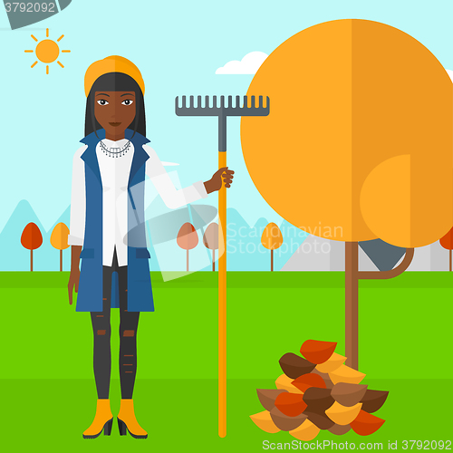 Image of Woman with rake near tree and heap of leaves.