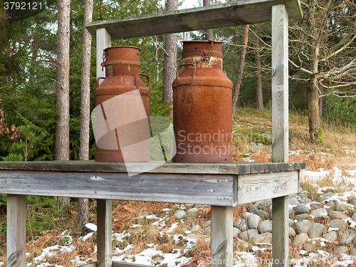 Image of two old rusty milk jug on a bench