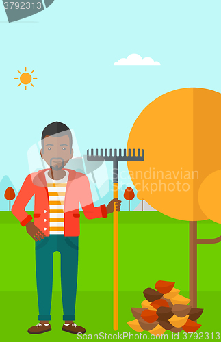 Image of Man with rake near tree and heap of leaves.