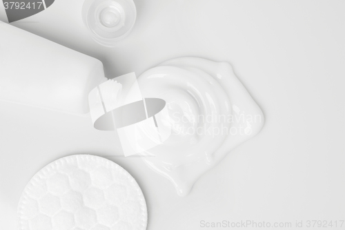 Image of splash of white cream, tube and cosmetic cotton disk