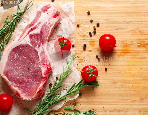 Image of Pieces of crude meat with rosemary and tomatoes.