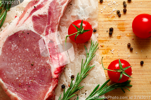 Image of Pieces of crude meat with rosemary and tomatoes.