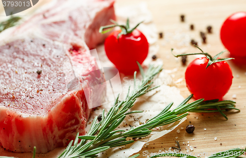 Image of Pieces of crude meat with rosemary and tomatoes.