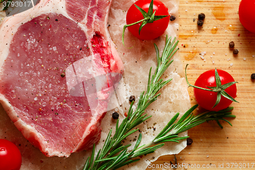 Image of Pieces of crude meat with rosemary and tomatoes.