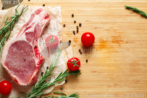 Image of Pieces of crude meat with rosemary and tomatoes.