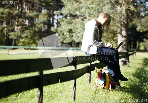 Image of Young woman sitting on a rustic fence