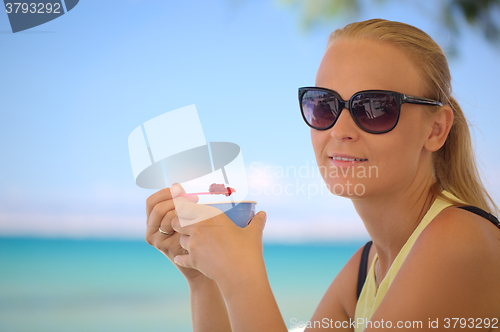 Image of Young woman eating ice-cream on the beach