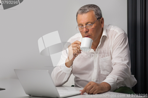 Image of Businessman drinking coffee while working in office