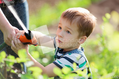 Image of Little boy playing with a jet of water in garden