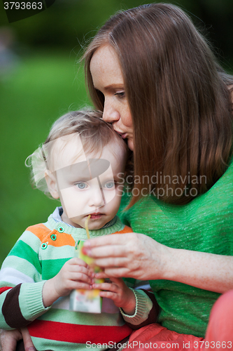 Image of Mother kissing the child drinking juice outdoor