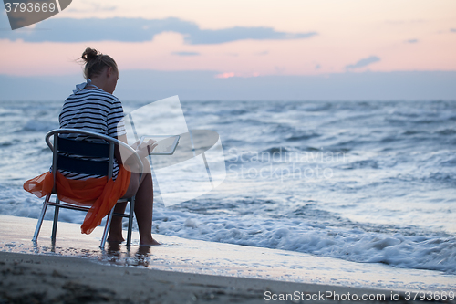 Image of Woman sitting on chair by sea and using pad