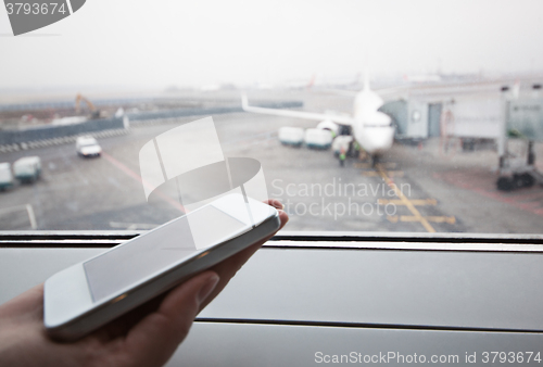 Image of Hand with smart phone by the window at airport