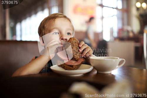 Image of Little child having lunch with sandwich and tea in cafe