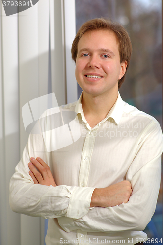 Image of Young smiling man with folded arms by the window