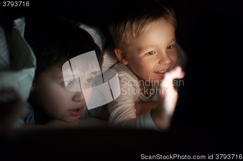 Image of Two boys watching movie or cartoon on pad at night