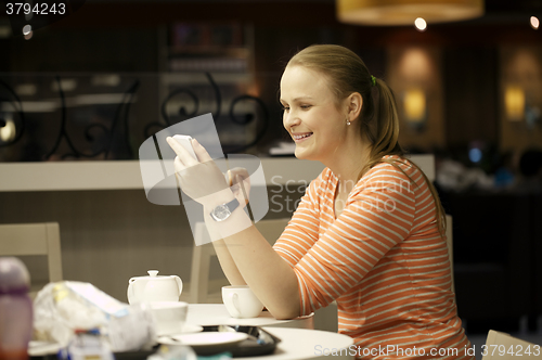 Image of Young woman chatting on smartphone in cafe.