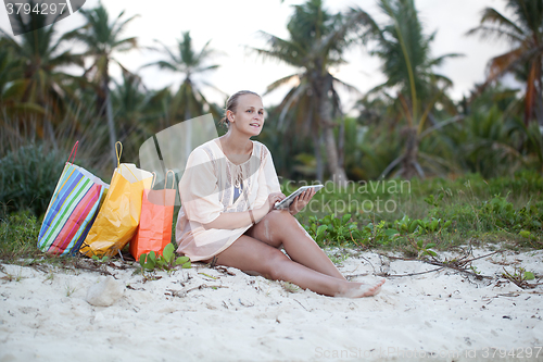 Image of Woman relaxing with pad on beach after shopping