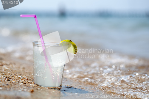 Image of Glass of lemonade or water on beach by sea