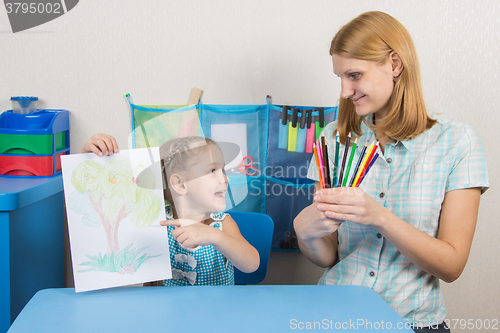 Image of Five-year girl showing on the picture and looked at my mother who is holding in the hands of colored pencils