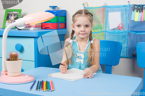 Image of Five-year girl draws pencil in a notebook and looked into the frame