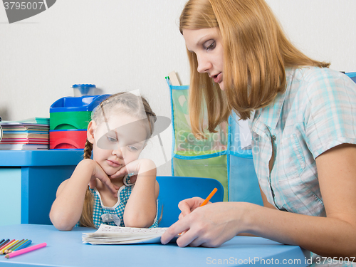 Image of Five-year girl with interest looking notebook and listening to the explanation of the teacher