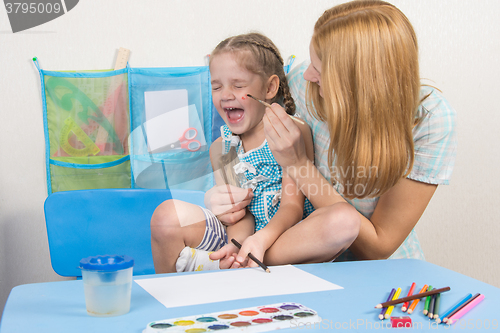 Image of Mother tickles the cheek with a brush to paint his daughter, five-year