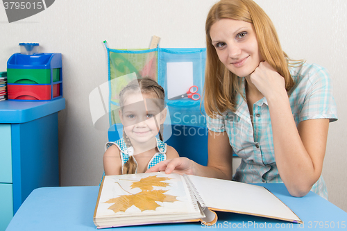 Image of Five-year girl and mother looking at the herbarium of the leaves in the album and looked in the frame