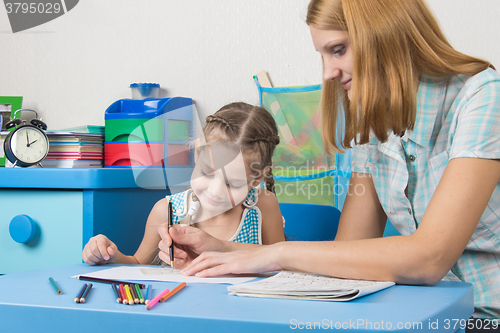 Image of A teacher helps a five-year girl with a ruler to draw