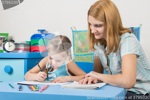 Image of The girl draws in a notebook with a ruler, the teacher helps her