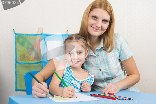Image of Five-year girl and young mother together paint a picture on a sheet of paper