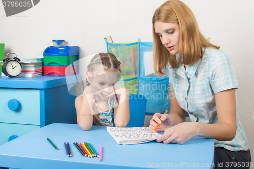 Image of Five-year girl with interest looks at the teaching material explained by an adult