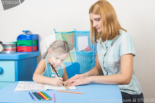 Image of Young girl helps a five-year girl draw a straight line with a ruler