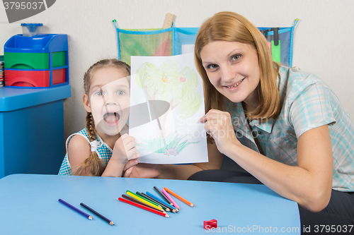 Image of Five-year girl and the teacher happily show drawn on a sheet of wood