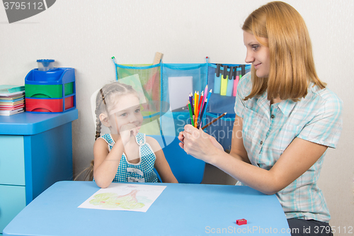 Image of Five-year girl choose the right pencil from the teacher hands