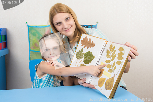 Image of Five-year girl and mother examining herbarium shows on one of the sheets in the album, and looked into the frame