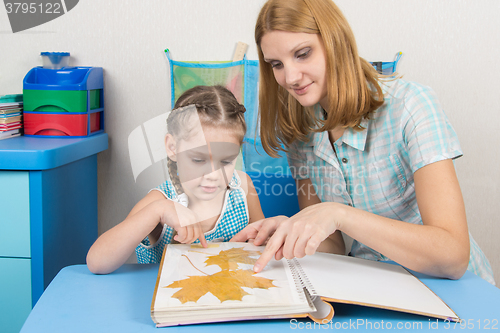 Image of Five-year girl and mother are considering the herbarium of the leaves in the album