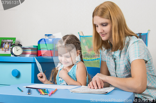 Image of Girl enjoys painting with teacher in kindergarten