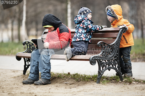 Image of Three young boys playing on a park bench in winter