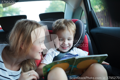 Image of Boy holding book sitting in a car with mother