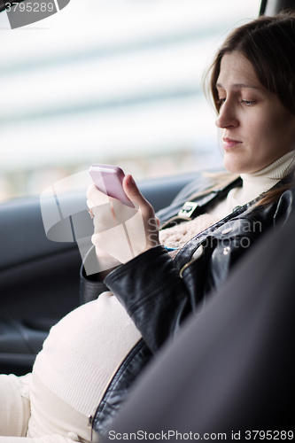 Image of Pregnant woman texting on cell in the car