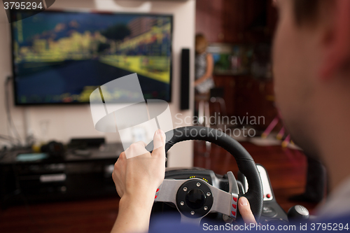 Image of Man playing racing game with steering wheel simulator