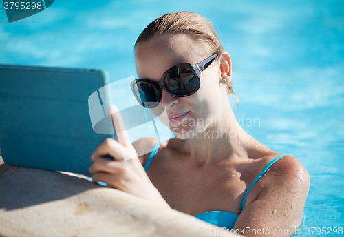 Image of Young woman using a tablet poolside