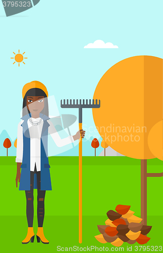 Image of Woman with rake near tree and heap of leaves.