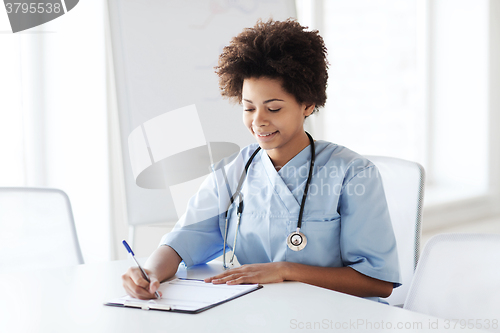 Image of happy female doctor or nurse writing to clipboard