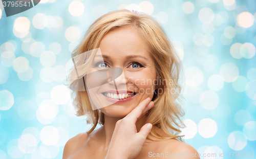 Image of smiling woman with bare shoulders touching face